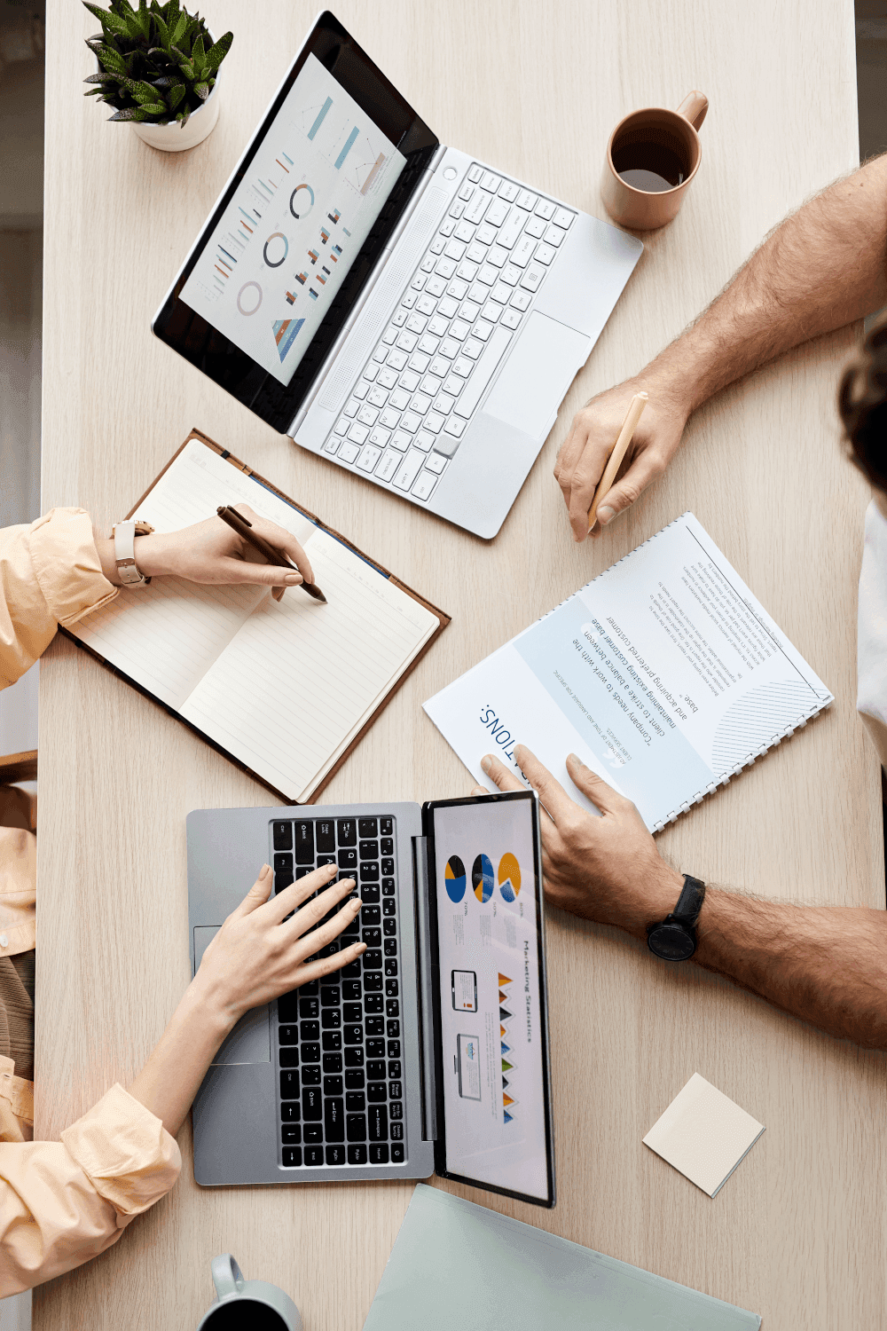Overhead view of people collaborating around a table with laptops and documents.