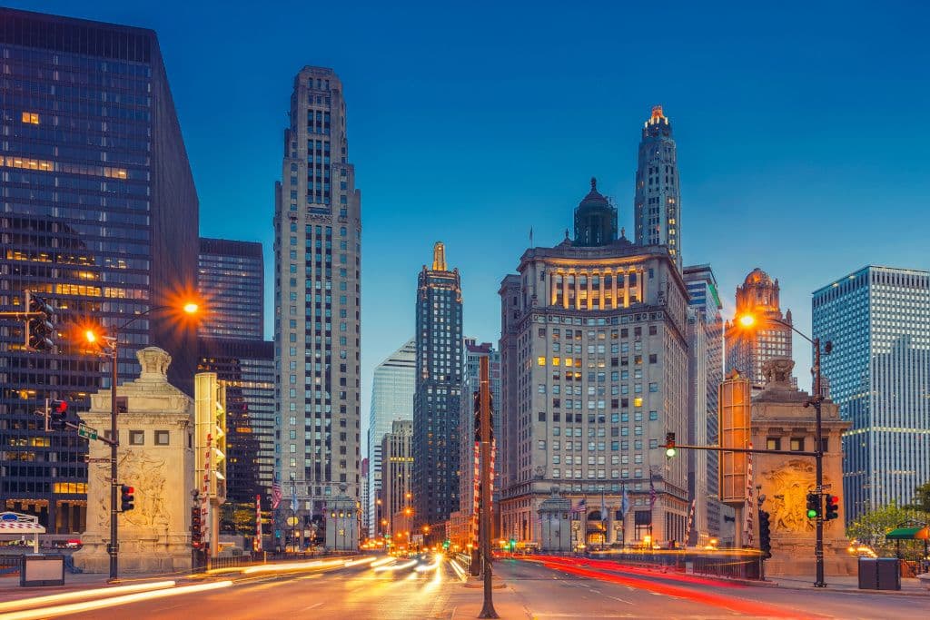 Chicago city skyline at night with illuminated skyscrapers and streaking car lights on the street.