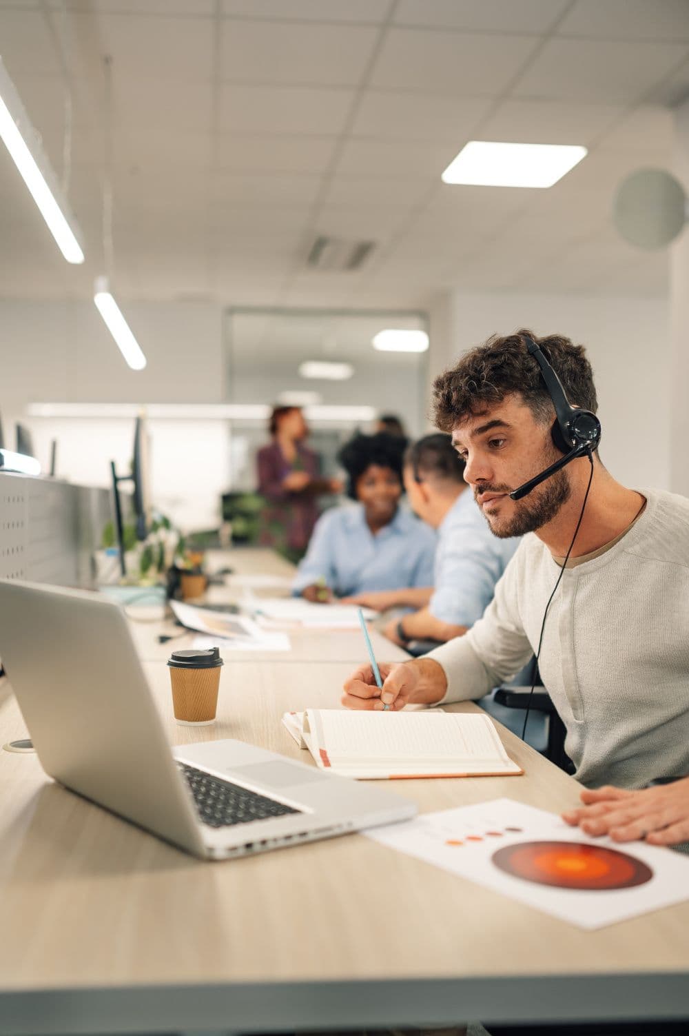 Man with headset works on laptop in a modern office, providing customer support.