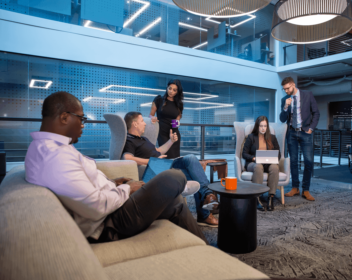 Diverse professionals collaborate in a modern, brightly lit office lounge with comfortable seating.