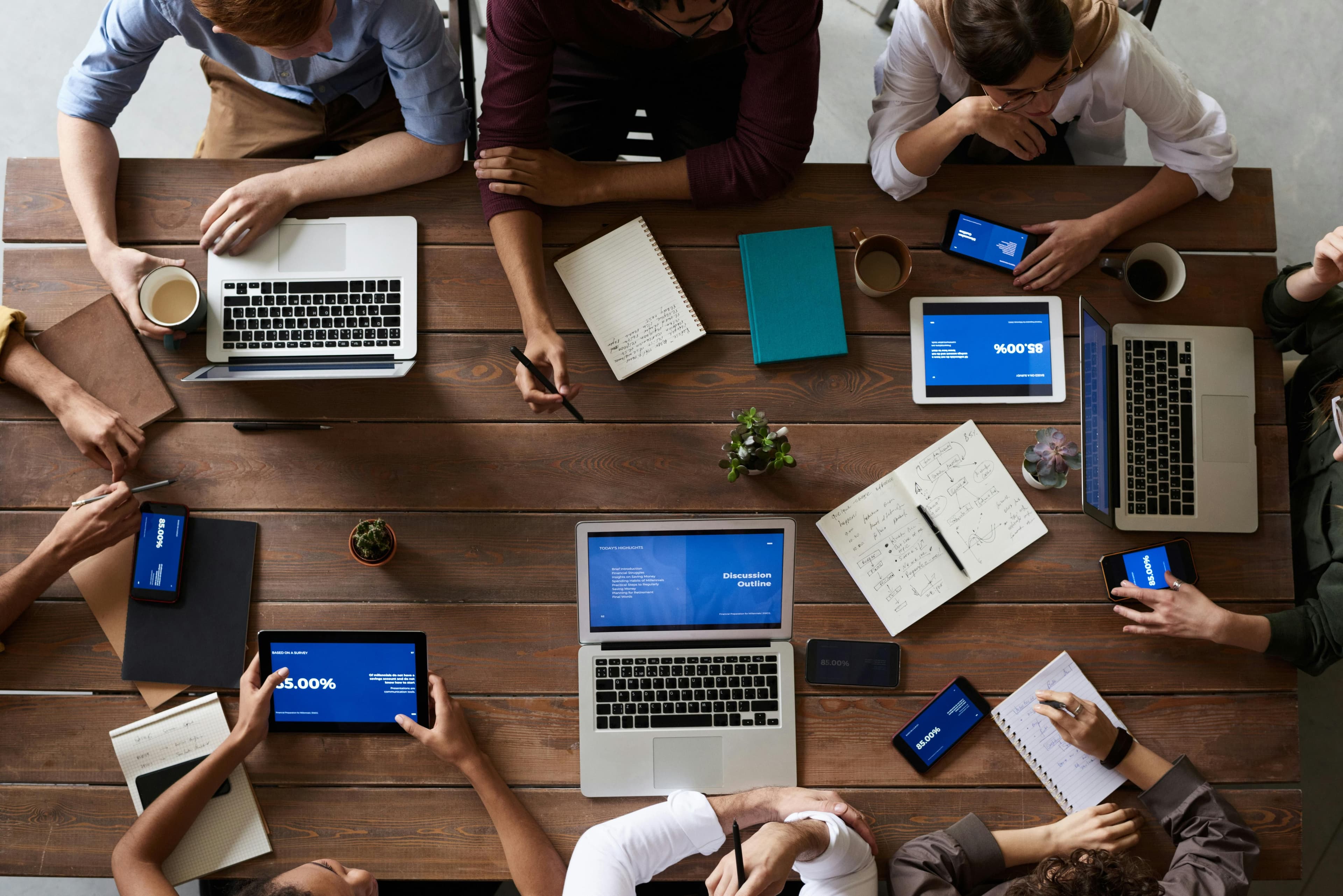 Overhead view of diverse people collaborating with laptops and tablets at a large wooden table.