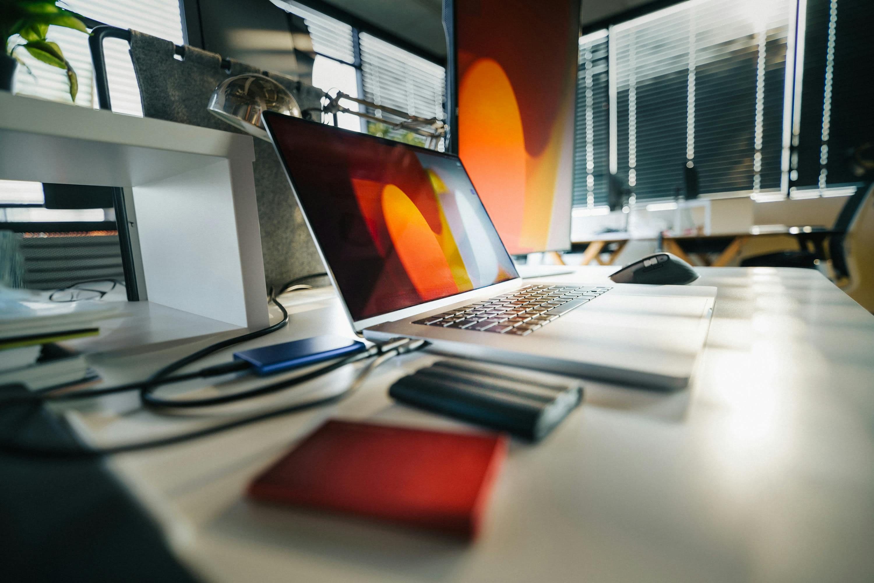 Laptop displaying abstract art on a modern office desk with external hard drives.
